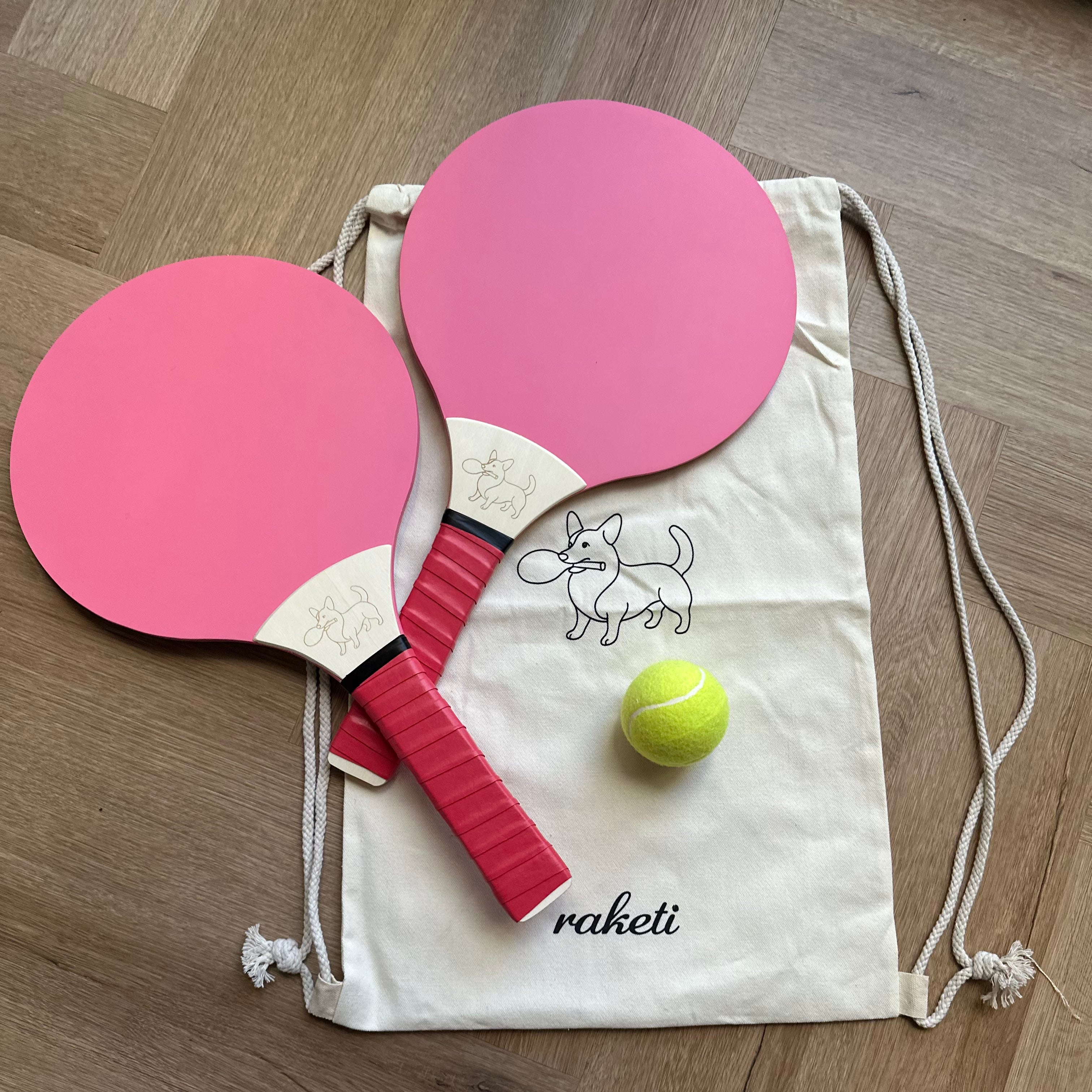 Two wooden paddle tennis rackets pink and red with a drawstring bag and ball
