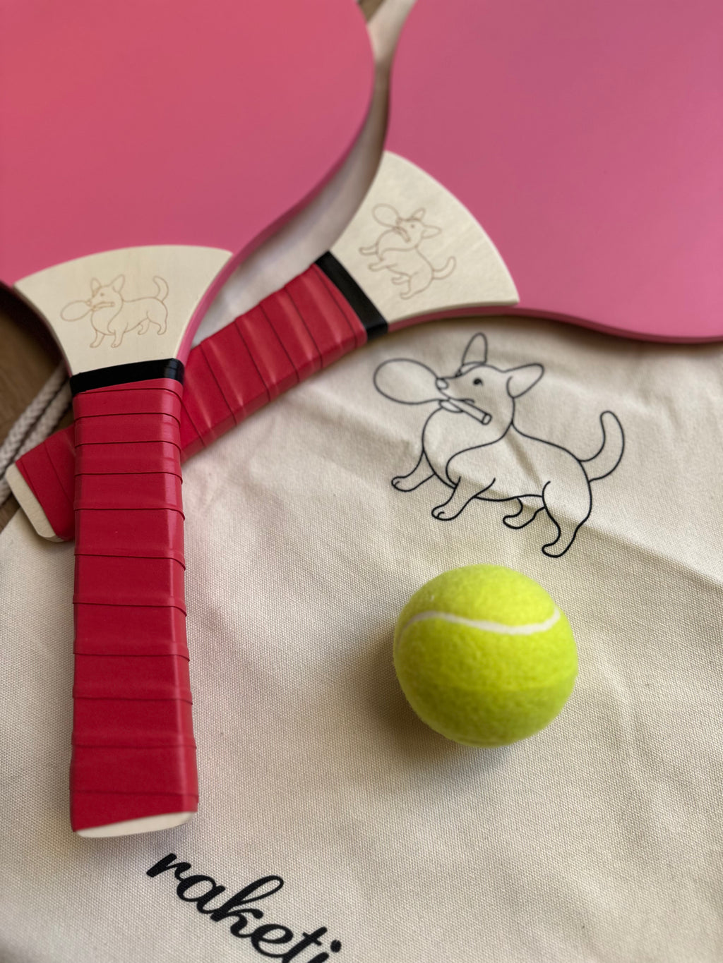 Two wooden paddle tennis rackets pink and red with a drawstring bag and ball